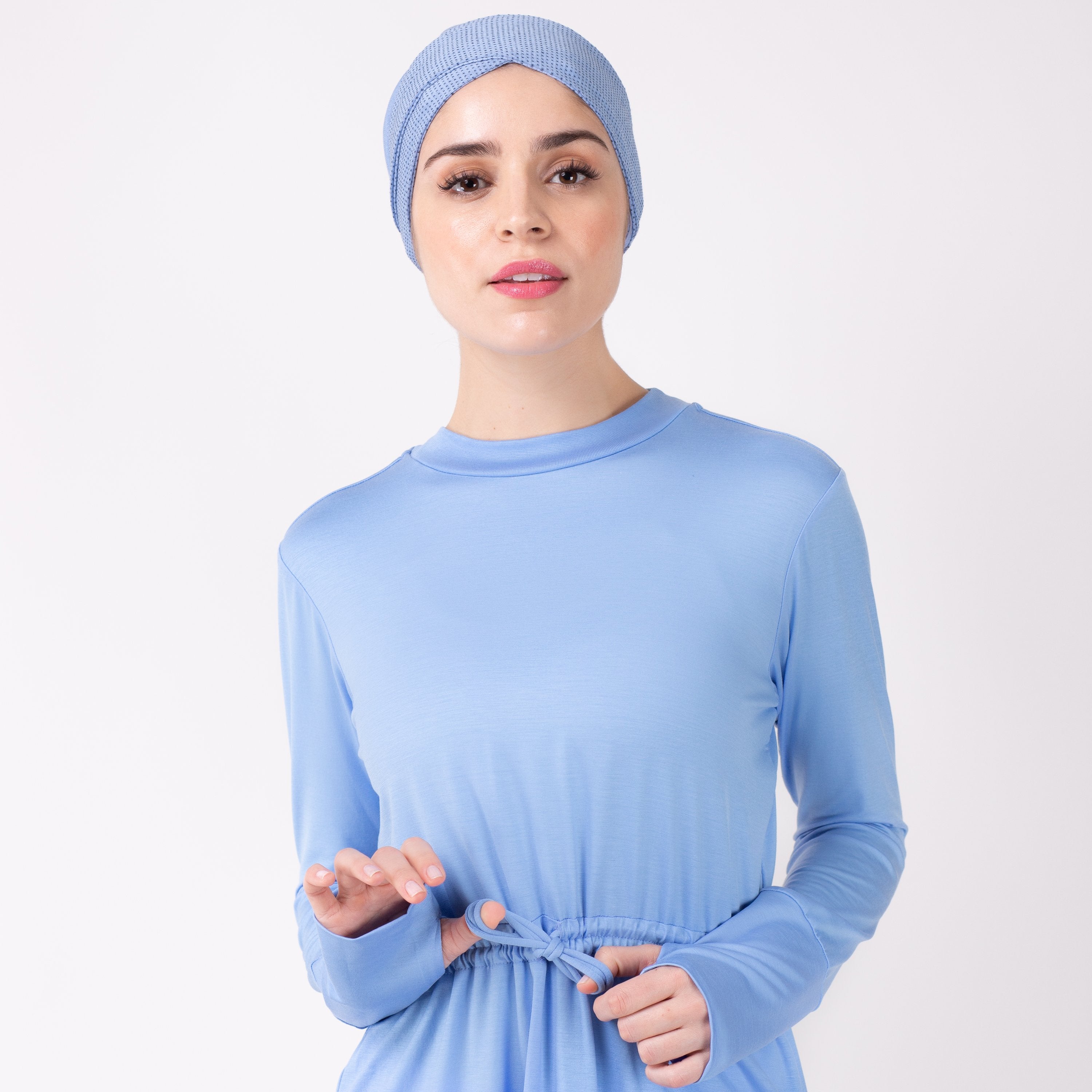 Close up of woman tying the modest, sky blue HAWA drawstring tee shirt against a white back drop.