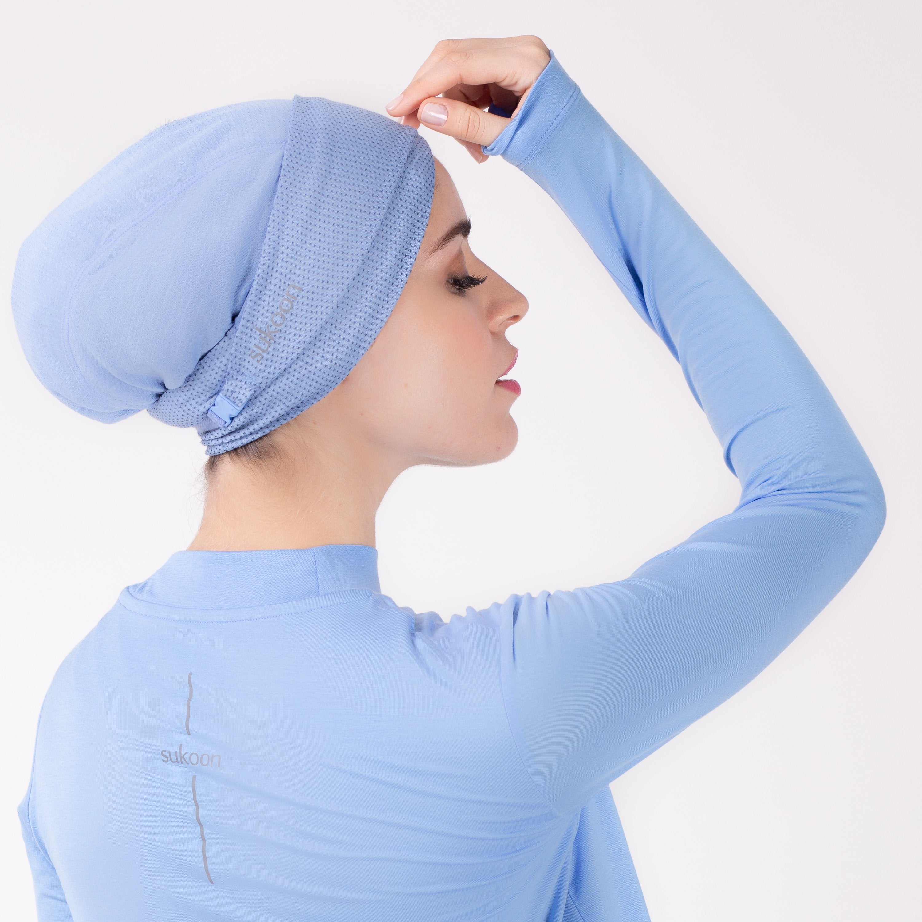 Right detail of woman in a sky blue shirt with matching sky blue HAWA headwrap with hand touching forehead.