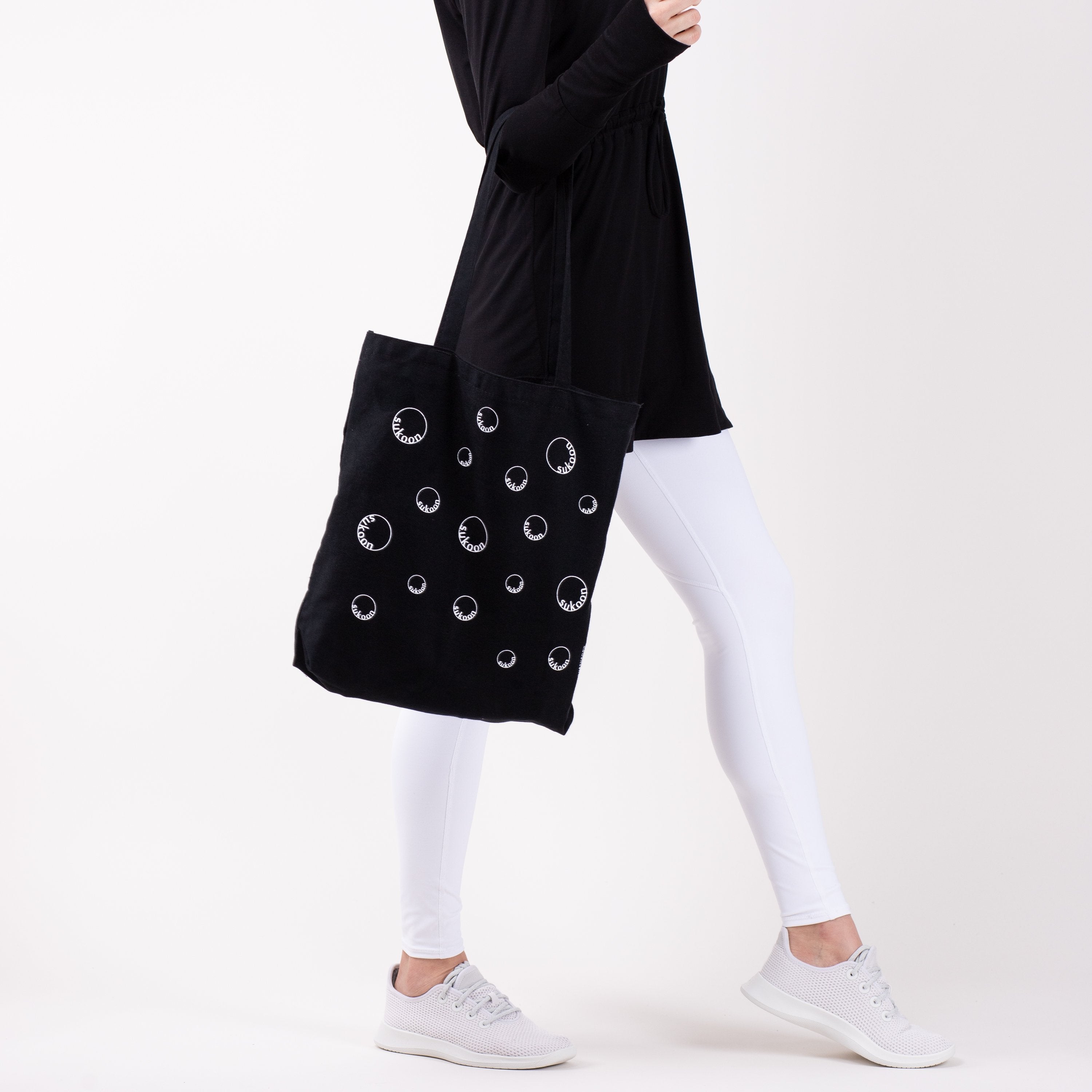 Woman with black tote bag with moon print in the crook of her elbow.
