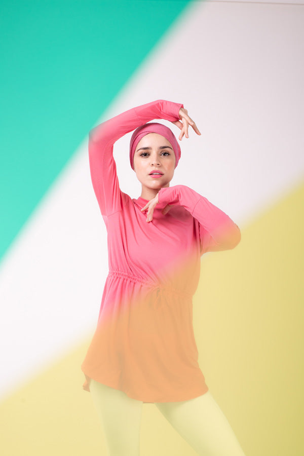 Woman in pink HAWA drawstring tee and a pink HAWA headwrap with one hand under her chin and one arm over her head.
