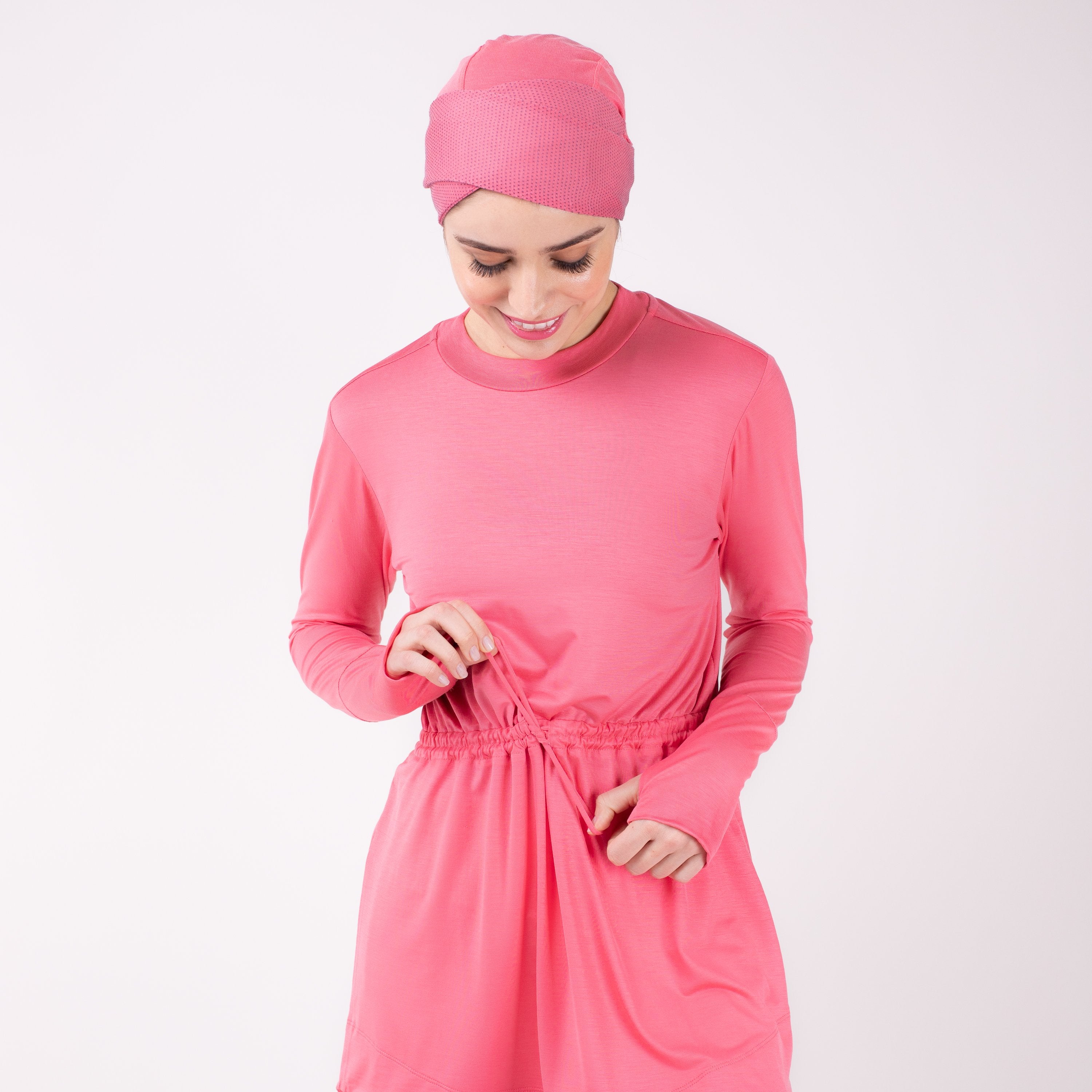 Close up of woman tying the modest, berry pink HAWA drawstring tee shirt with her head bent against a white back drop.