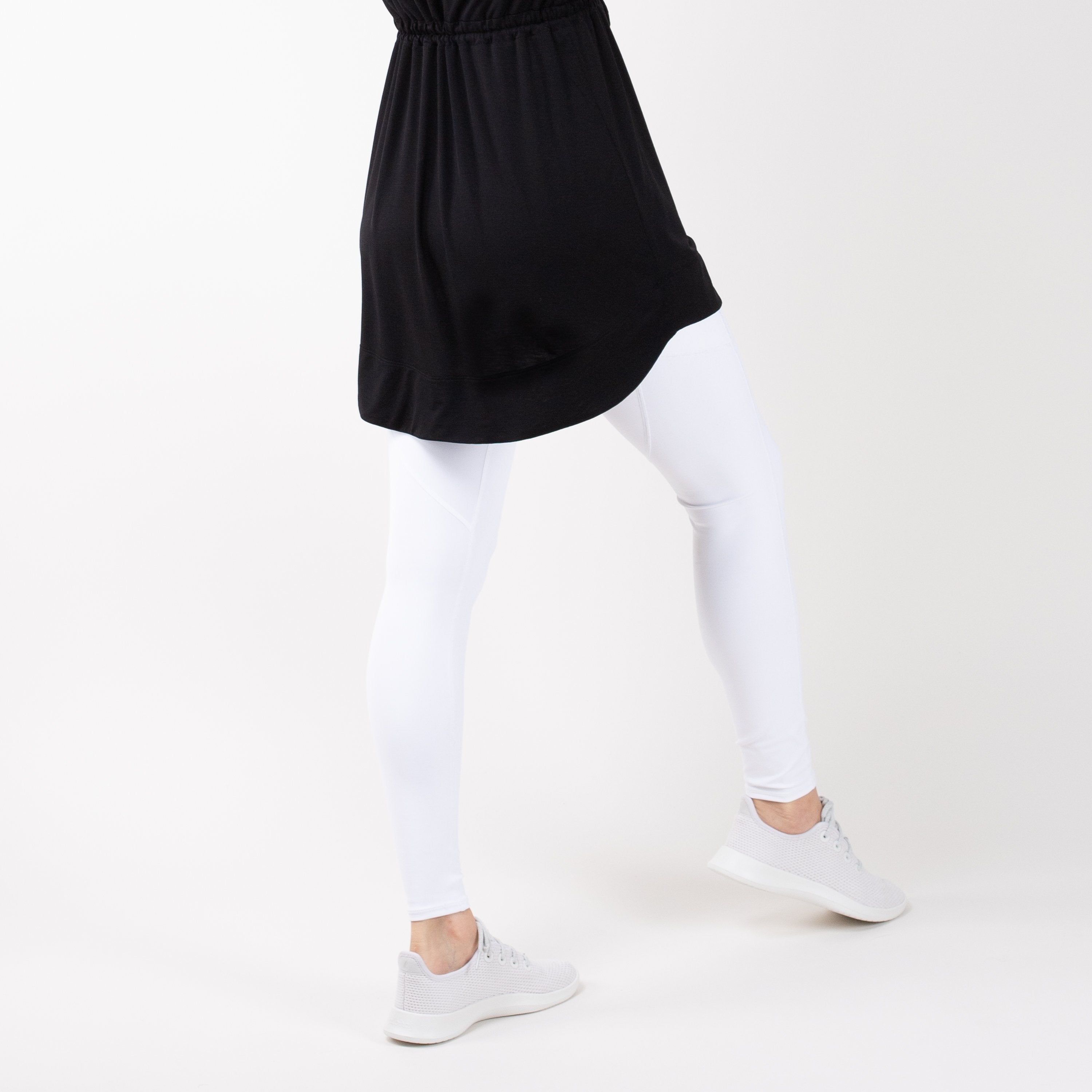Detail shot of lower-half of a woman in modest, black HAWA drawstring tee shirt and white leggings in front of a white backdrop.