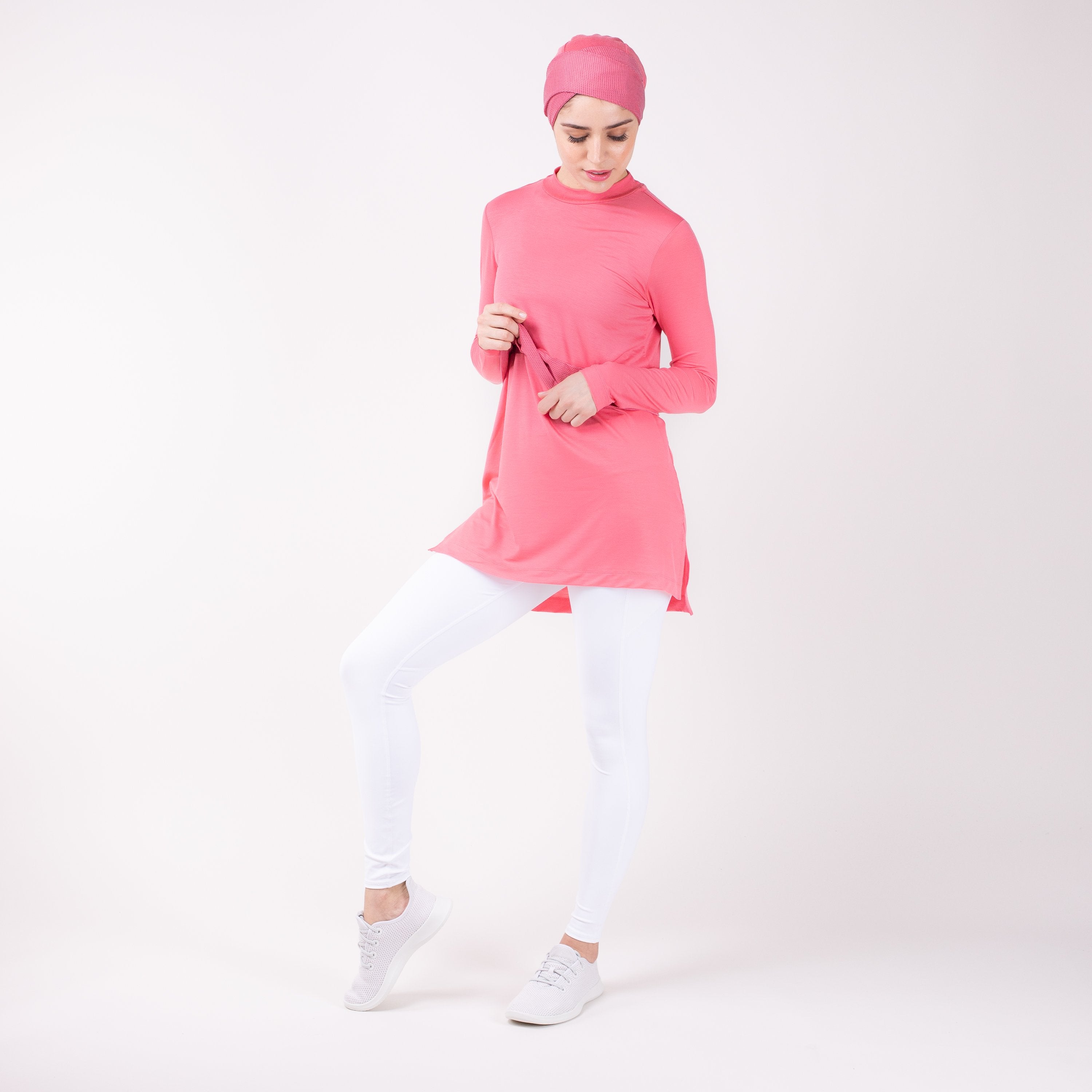 Woman in pink HAWA Step Tee with both hands in front of her body and right leg popped.