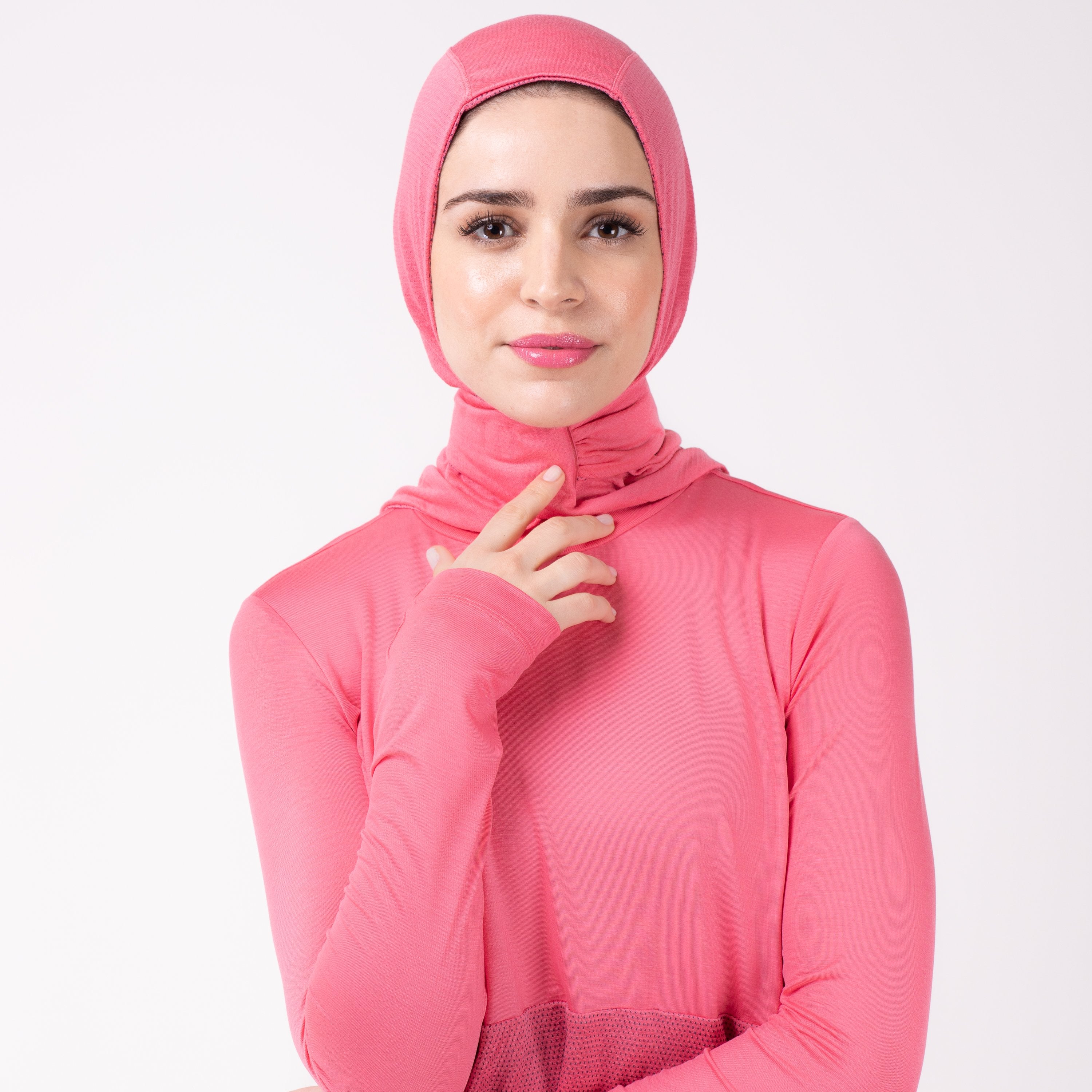 Front detail of a woman in a pink shirt with a matching pink HAWA hijab, touching the closure with her right hand.