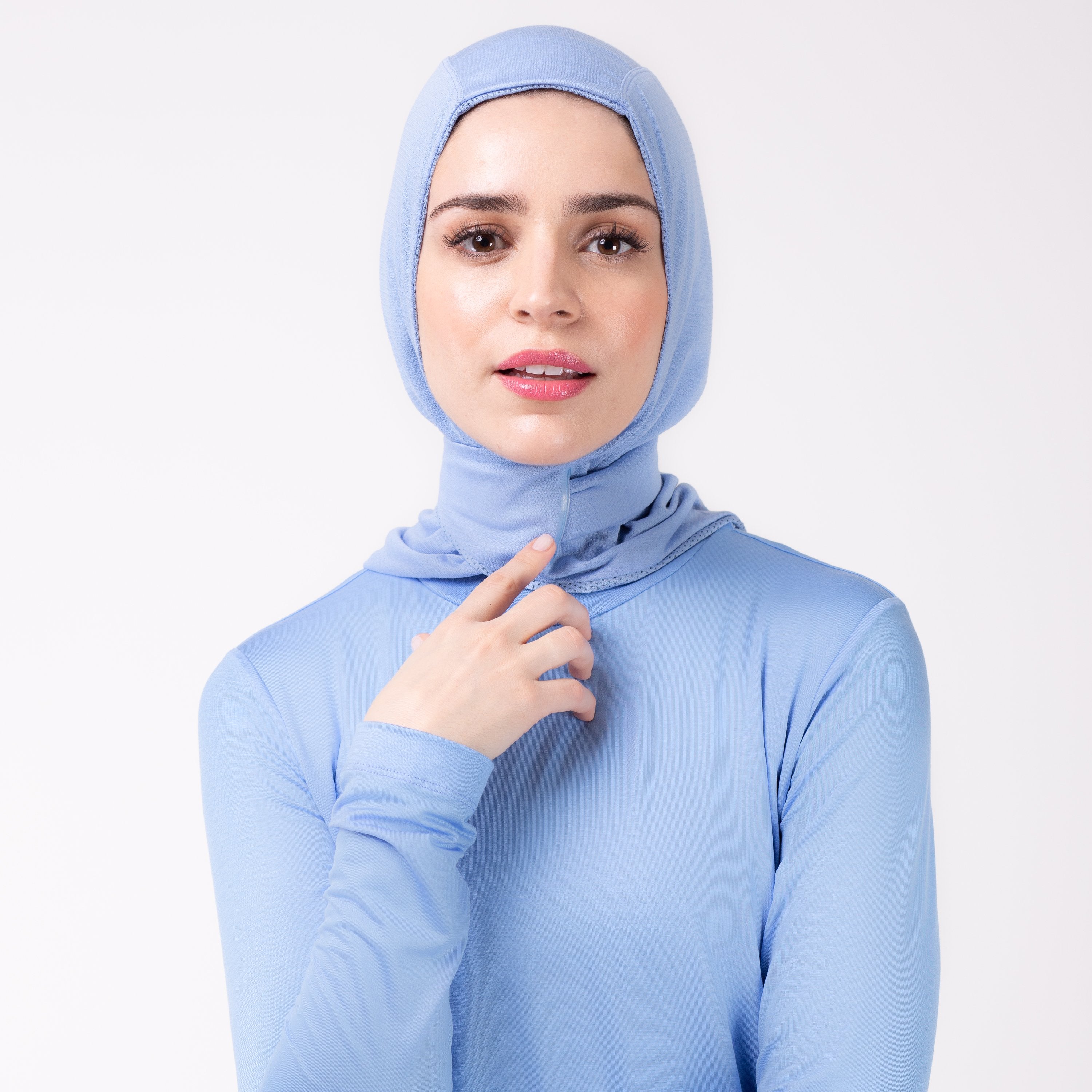 Front detail of a woman in a sky blue shirt with a matching sky blue HAWA hijab, touching the closure with her right hand.