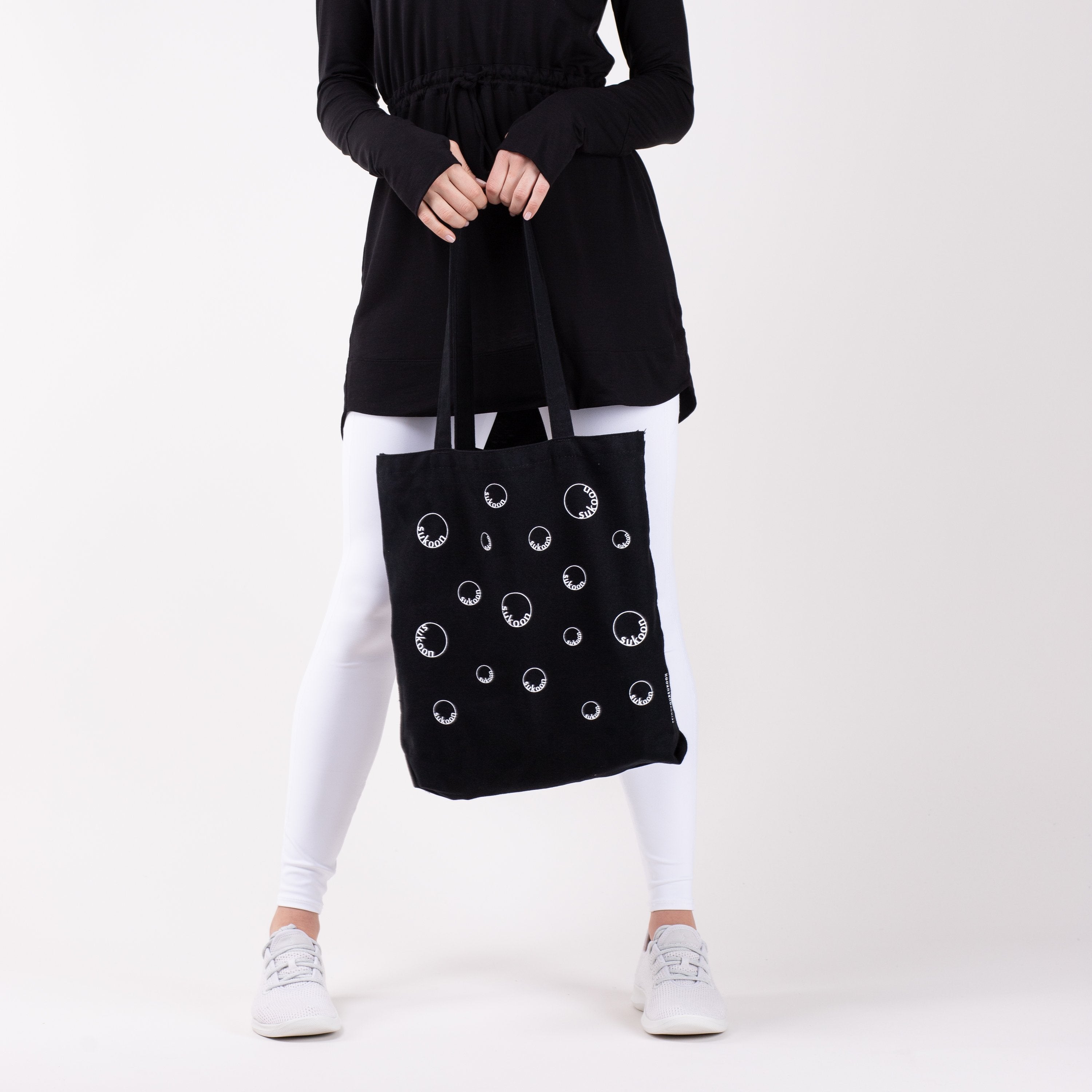 Woman holding black tote bag with moon print in front of her.